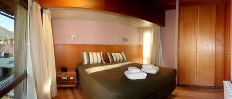 A hotel room with a bed, pillows, a nightstand, a telephone, and a wooden wardrobe.