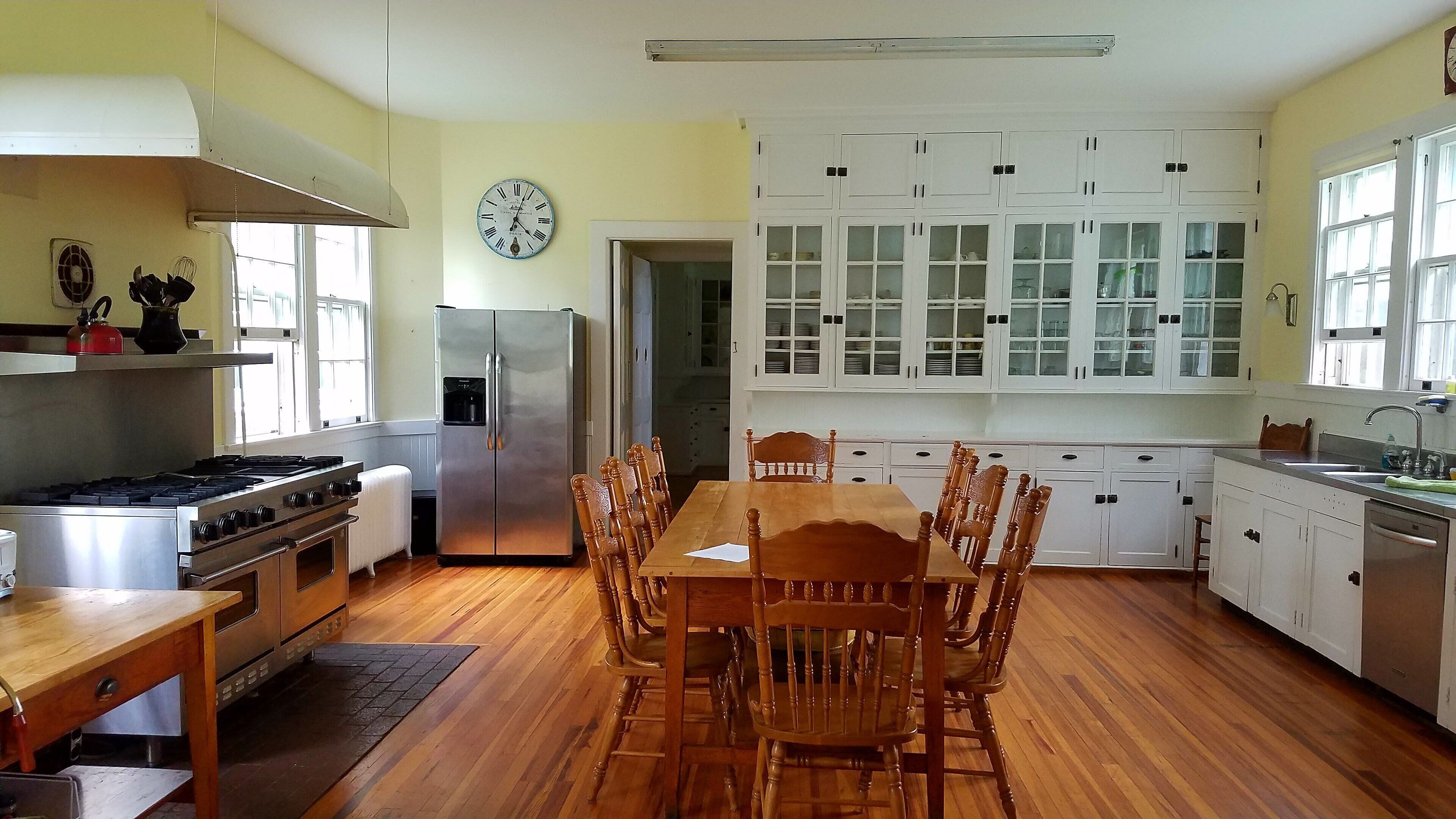 A kitchen with wooden flooring, a dining table with chairs, a refrigerator, a stove, and cabinets.