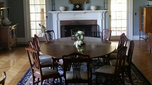 A dining room with a round table surrounded by chairs, a fireplace, and a large window. - Vacation Like Gatsby on This Historic 500-Acre Fairy Tale Estate  (Gilbertsville)
