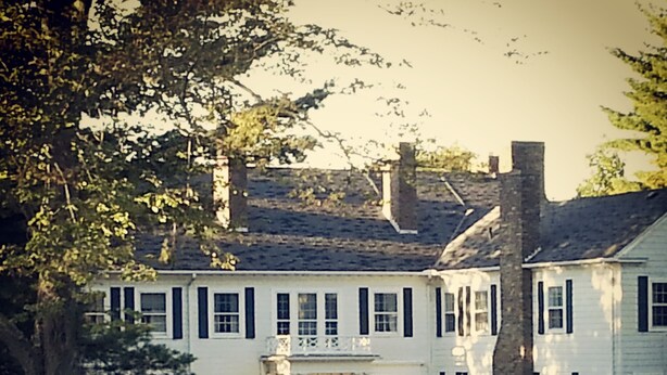 A large, two-story white building with black shutters, a central entrance, and a well-maintained lawn. - Vacation Like Gatsby on This Historic 500-Acre Fairy Tale Estate  (Gilbertsville)