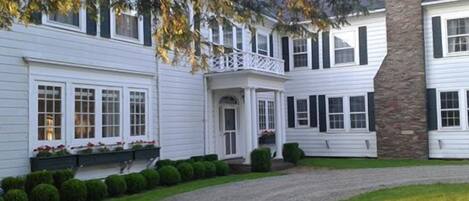 A two-story white house with a stone chimney, a covered porch, and a gravel driveway.