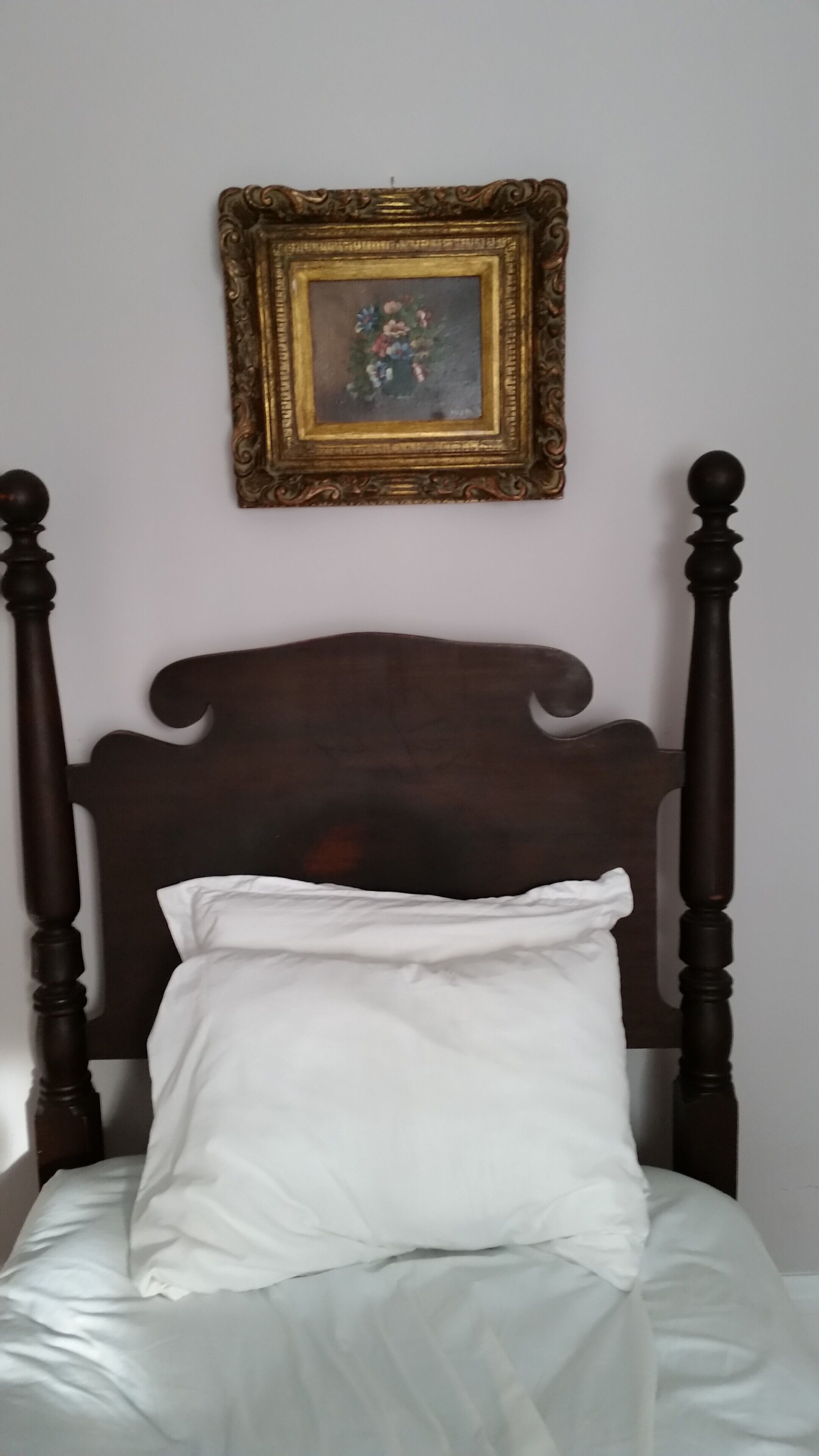 A bed with a wooden headboard, a white pillow, and a framed picture on the wall above.