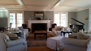 A spacious living room with a fireplace, two armchairs, a sofa, a piano, and a large window. - Vacation Like Gatsby on This Historic 500-Acre Fairy Tale Estate  (Gilbertsville)