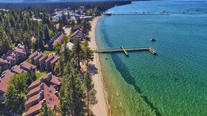 Vue aérienne d’une zone côtière avec une plage dégagée, une jetée en bois et des immeubles résidentiels aux toits inclinés.