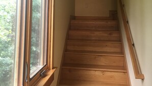 Una escalera de madera con barandilla que lleva a un rellano con ventana con vistas a la vegetación.