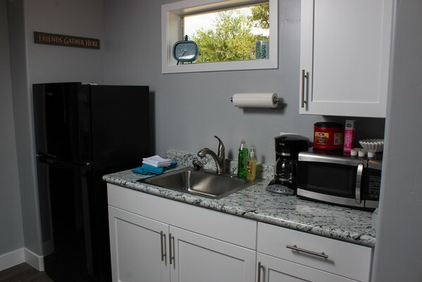 A kitchen with a sink, a refrigerator, a microwave, and a window with a view of trees.