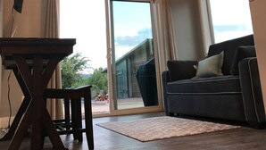 Un soggiorno moderno con una ventola a soffitto, un'ampia porta scorrevole in vetro che dà su uno spazio esterno, un divano scuro e un tavolo in legno.