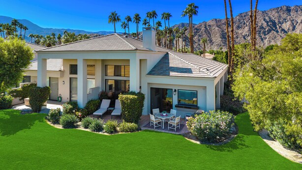A modern house with a patio, surrounded by lush greenery and palm trees, with mountains in the background. - Stay Where the Legends Play - Front Row Fairway Views at PGA West Stadium (La Quinta)