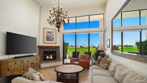A spacious living room with a large TV, fireplace, comfortable seating, and a view of a golf course. - Stay Where the Legends Play - Front Row Fairway Views at PGA West Stadium (La Quinta)