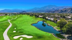 Ein Golfplatz mit Teich, umgeben von Bergen und Palmen.