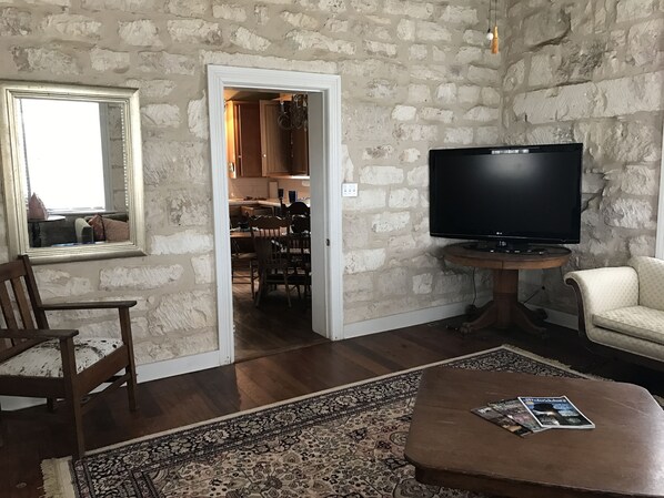 A living room with a stone wall, a TV, a coffee table with magazines, a chair, and a rug.
