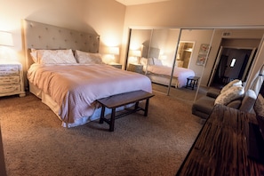 A bedroom with a bed, bedside tables, a bench, a mirror, and a wardrobe.