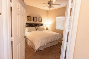 A bedroom with a bed, a ceiling fan, a nightstand, and a window with blinds.