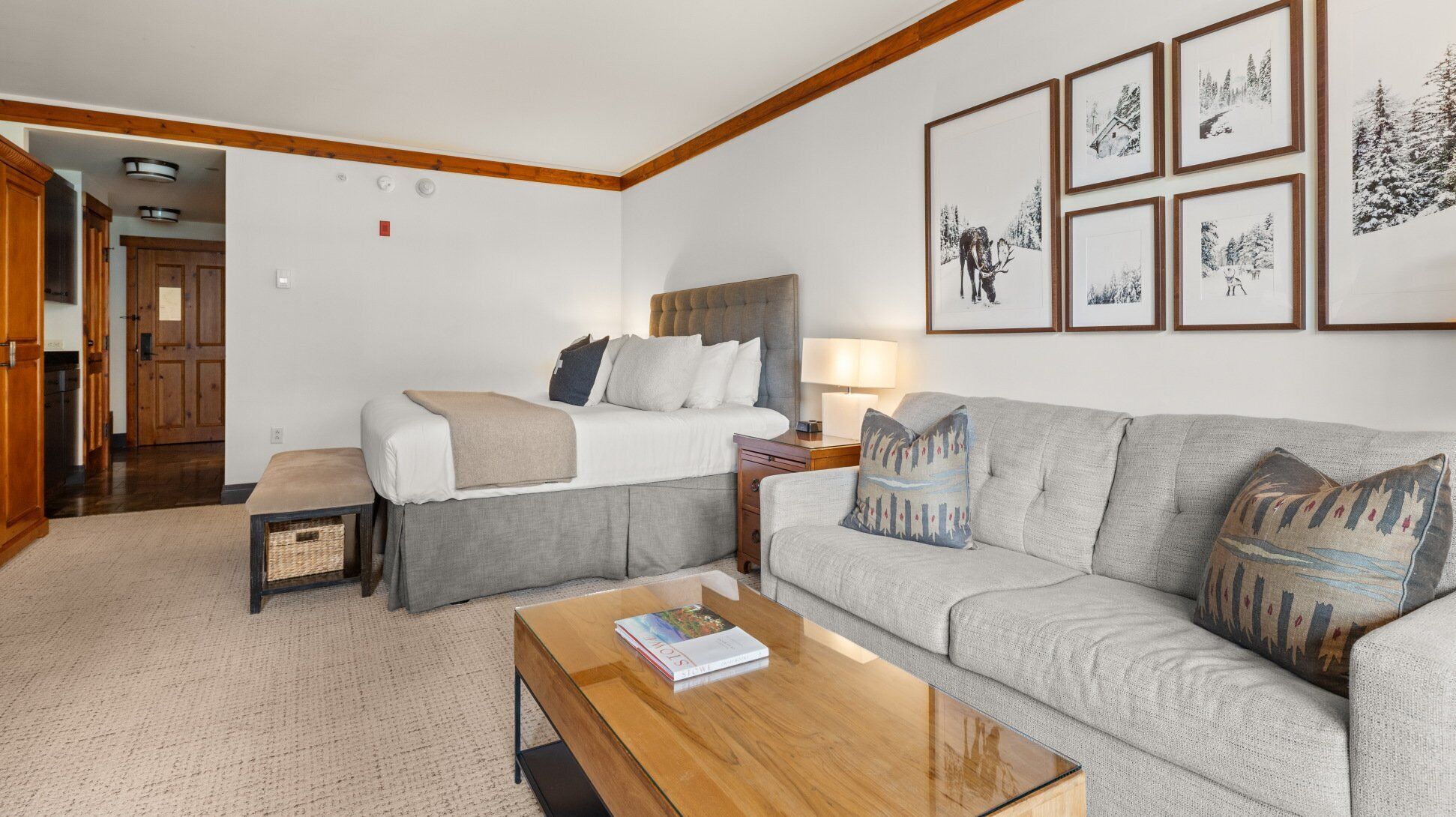A hotel room with a bed, a sofa, a coffee table, and framed pictures on the wall.