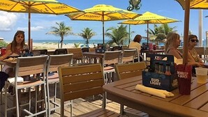 Ein Außenbereich mit Essplätzen, gelben Sonnenschirmen, Holztischen und -stühlen.