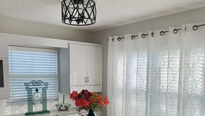 Ein Essbereich mit einem Holztisch, zwei Stühlen, einer Vase mit Blumen und einem Fenster mit Jalousien.