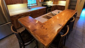 A kitchen with wooden cabinets, a stainless steel refrigerator, a double sink, and a wooden island with bar stools. - Beautiful, family-friendly home in private wilderness setting (Wilmington)