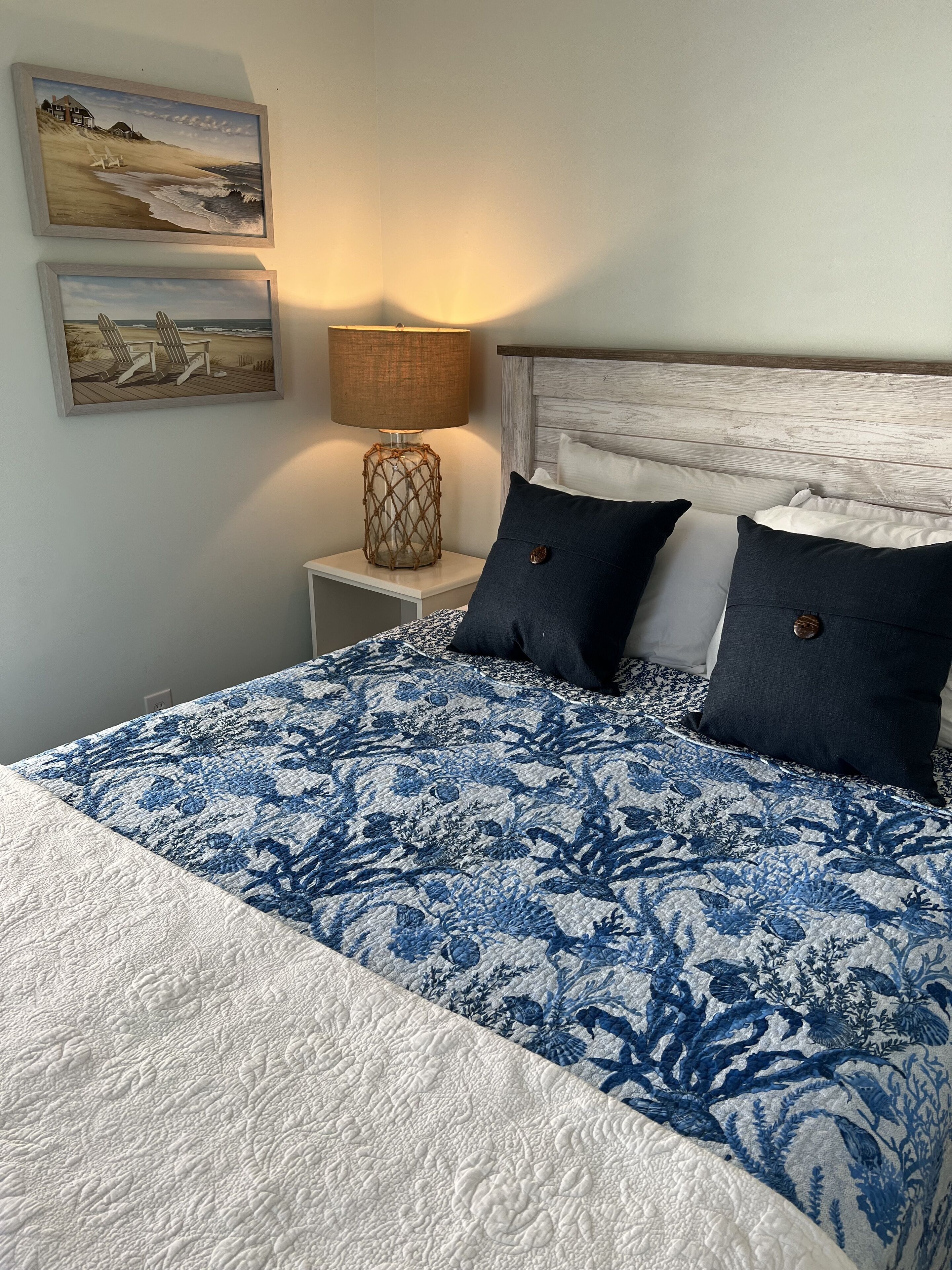 A bedroom with a bed, two pillows, a nightstand, a lamp, and two wall-mounted paintings.