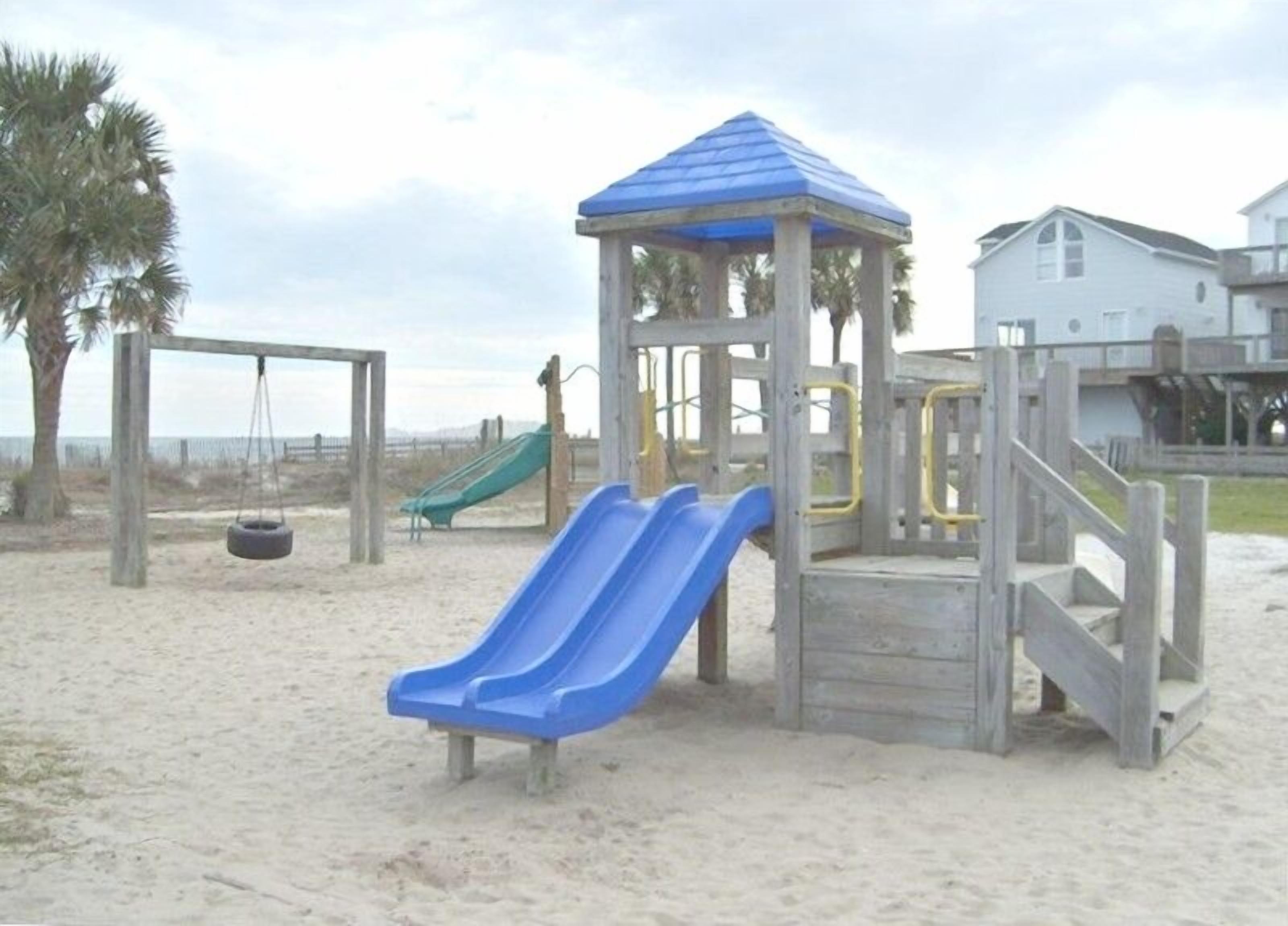 Une aire de jeux de plage avec un toboggan bleu et une balançoire.
