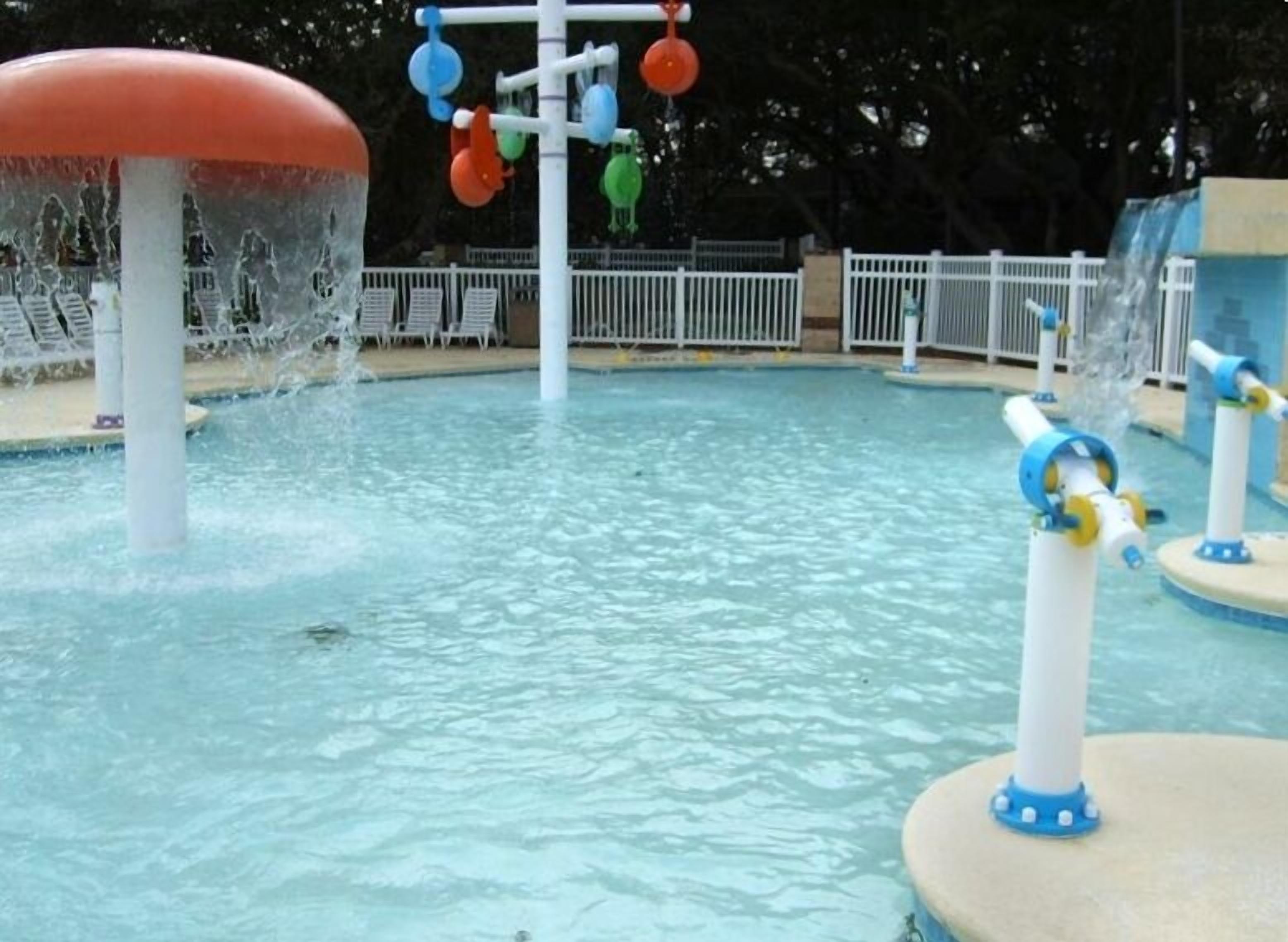 Ein Wasserspielbereich mit einer zentralen Wasserfontäne und bunten, hängenden Elementen.