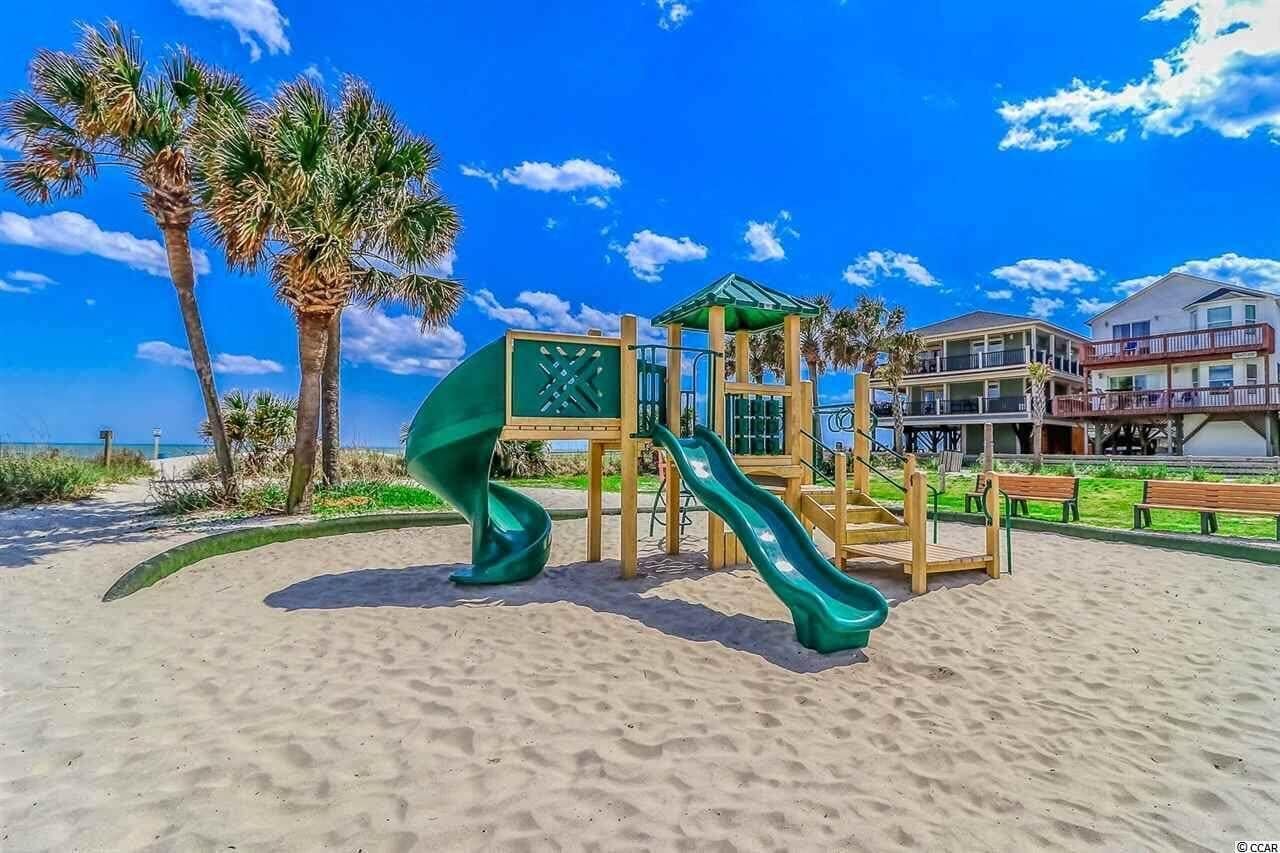 A beachside playground with a slide, palm trees, and a building in the background.