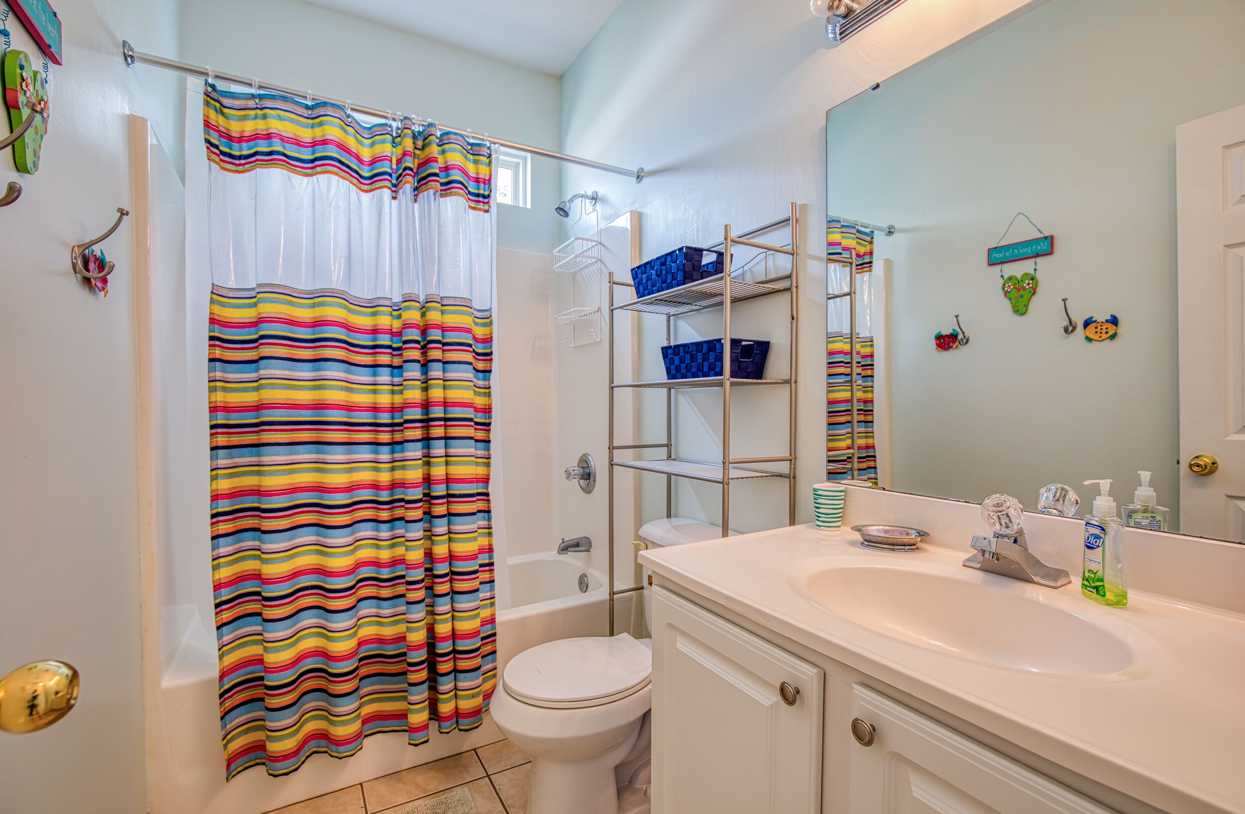 A bathroom with a striped shower curtain, a white bathtub, a toilet, a white sink with a mirror, and shelves with blue baskets.