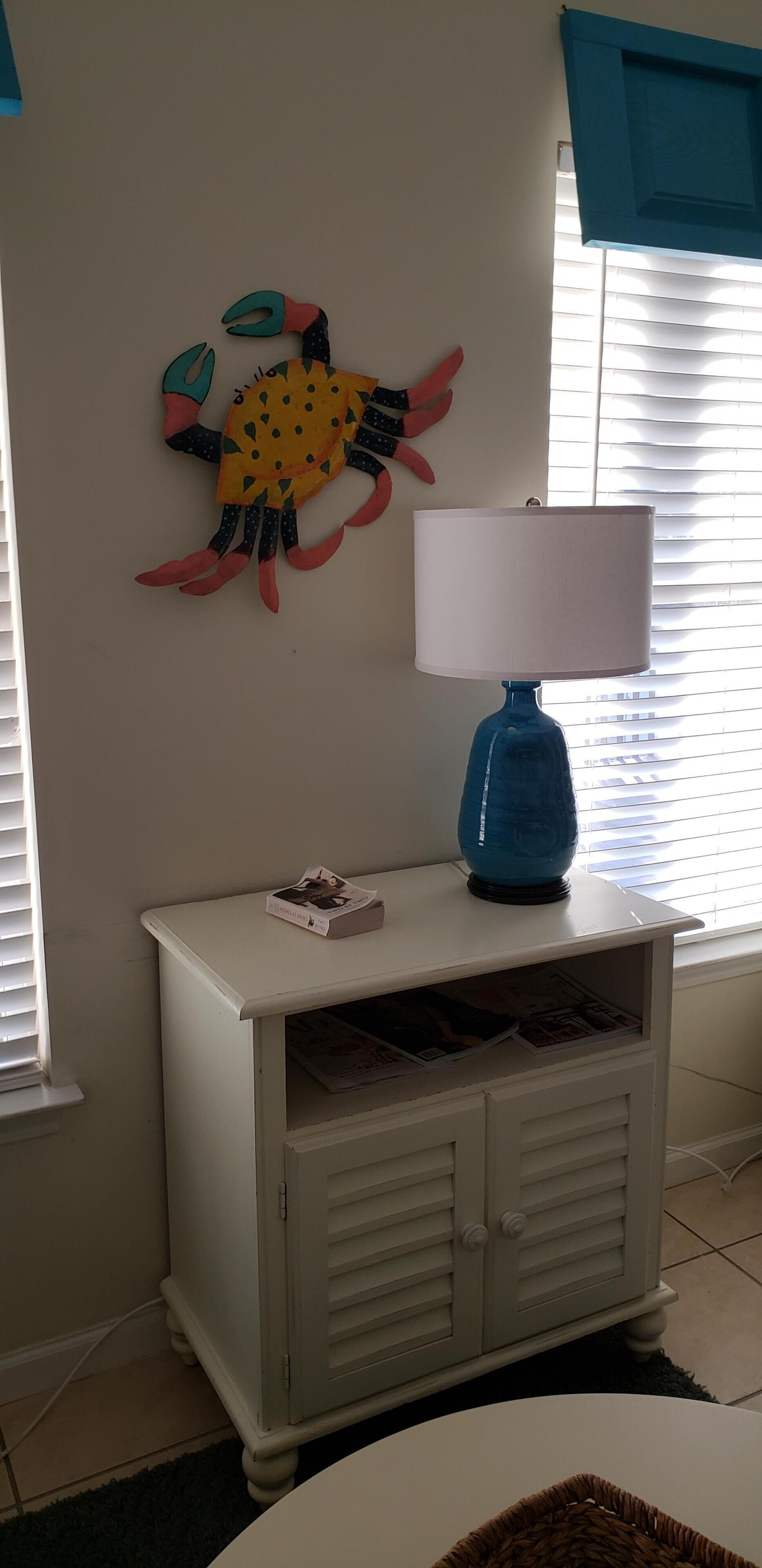 Un tavolo consolle bianco con una lampada blu, un'opera d'arte a tema granchio sulla parete e una rivista sul tavolo.