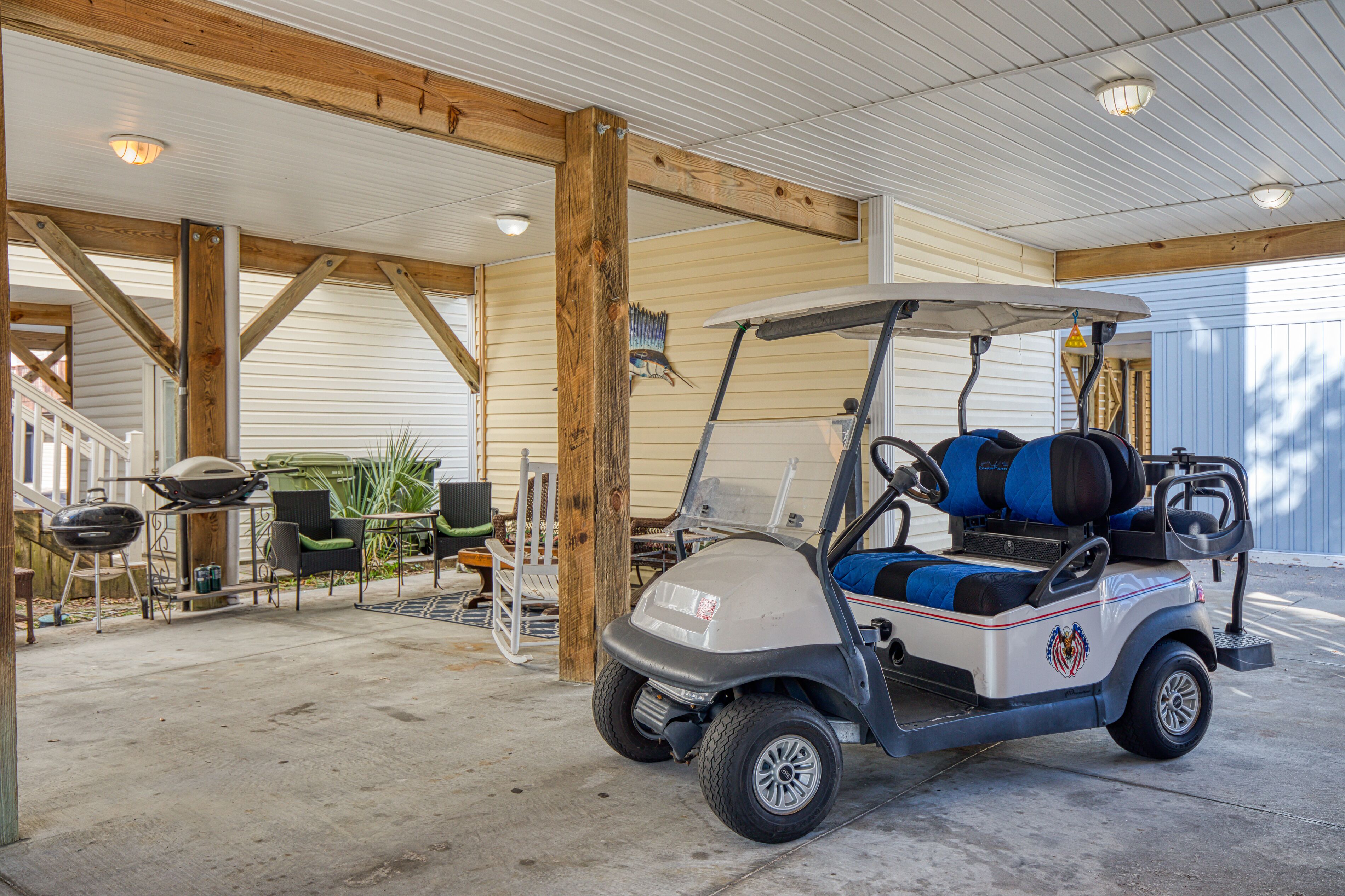 A golf cart in a covered garage with a concrete floor, wooden beams, and outdoor furniture.