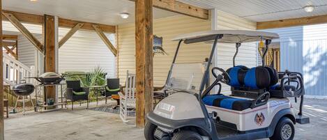 A golf cart in a covered garage with a concrete floor, wooden beams, and outdoor furniture.