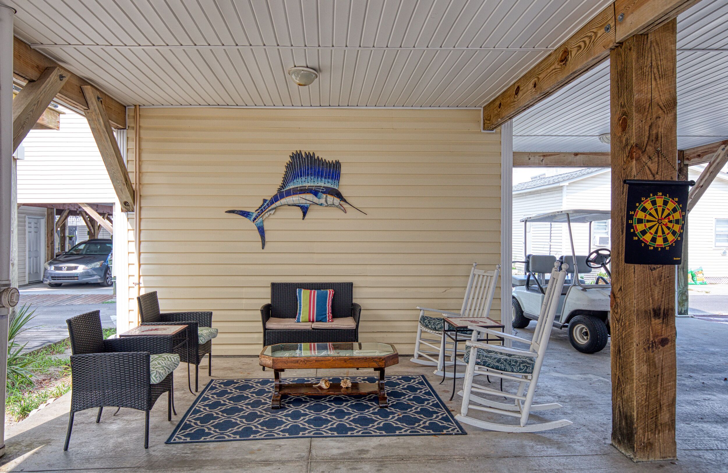 A covered outdoor seating area with wicker furniture, a glass coffee table, and a decorative fish mural on the wall.