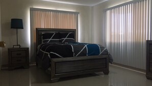 Une chambre à coucher avec un lit, des tables de chevet, une lampe et une fenêtre avec des stores.