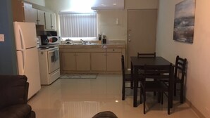 Une cuisine compacte équipée d’un réfrigérateur, d’un four à micro-ondes et d’une cuisinière, d’une table à manger avec des chaises et d’une fenêtre avec des stores.