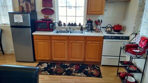 A compact kitchen with wooden cabinets, a stainless steel sink, a microwave, a stove, and a coffee maker.