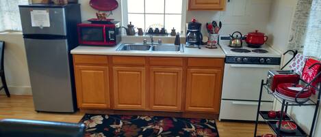 A compact kitchen with wooden cabinets, a stainless steel sink, a microwave, a stove, and a coffee maker.