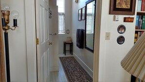 A hallway with a patterned rug, a wooden door, a small table with a basket, and a wall with framed pictures and a mirror.