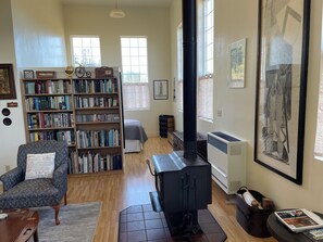 Un salon chaleureux avec une cheminée, des étagères à livres, un fauteuil confortable et une grande fenêtre laissant entrer la lumière naturelle.