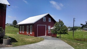 A red barn with a white roof, a large garage door, and a paved driveway leading to the entrance.