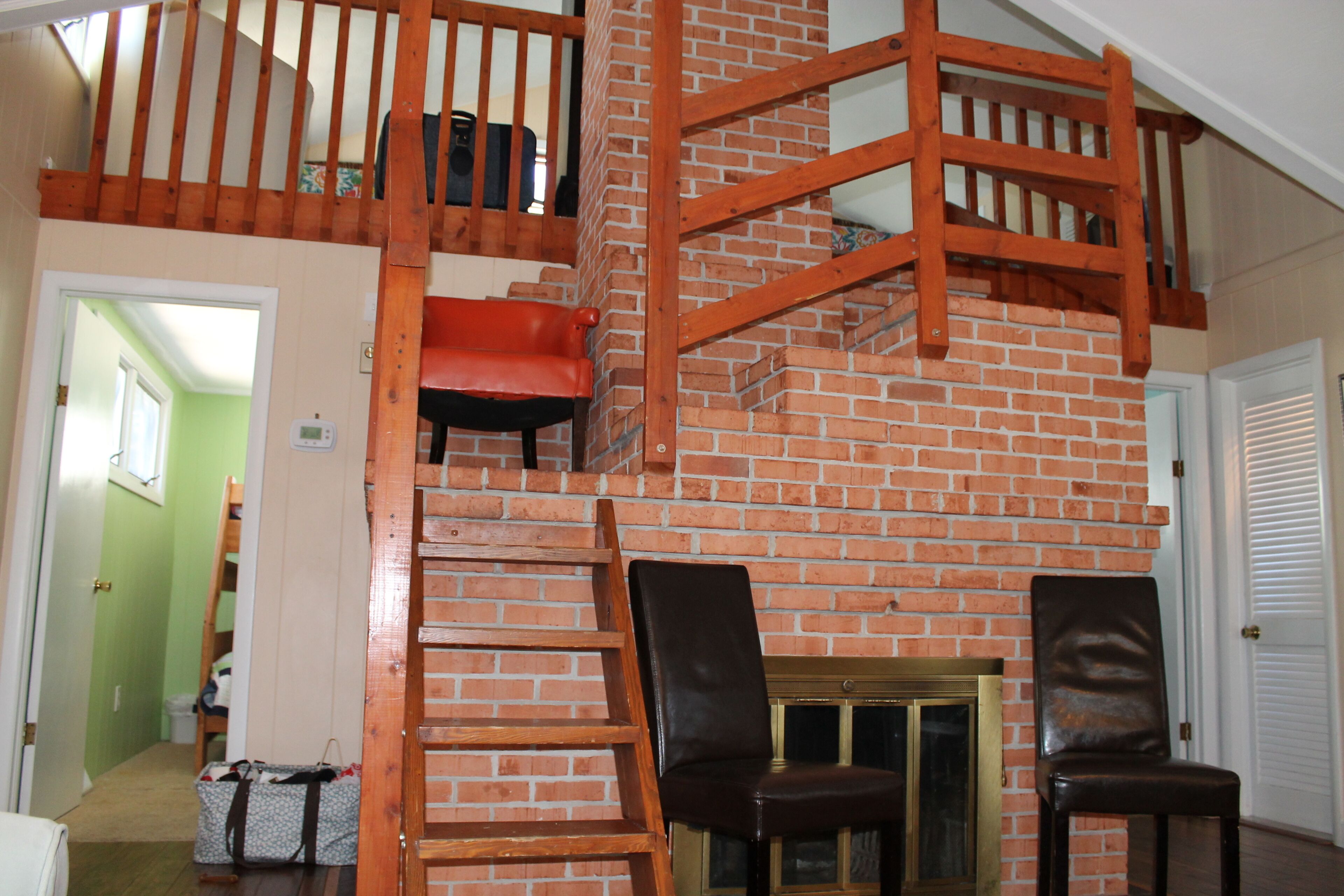 A multi-level wooden staircase with a brick wall backdrop, two leather chairs, and a small cabinet.