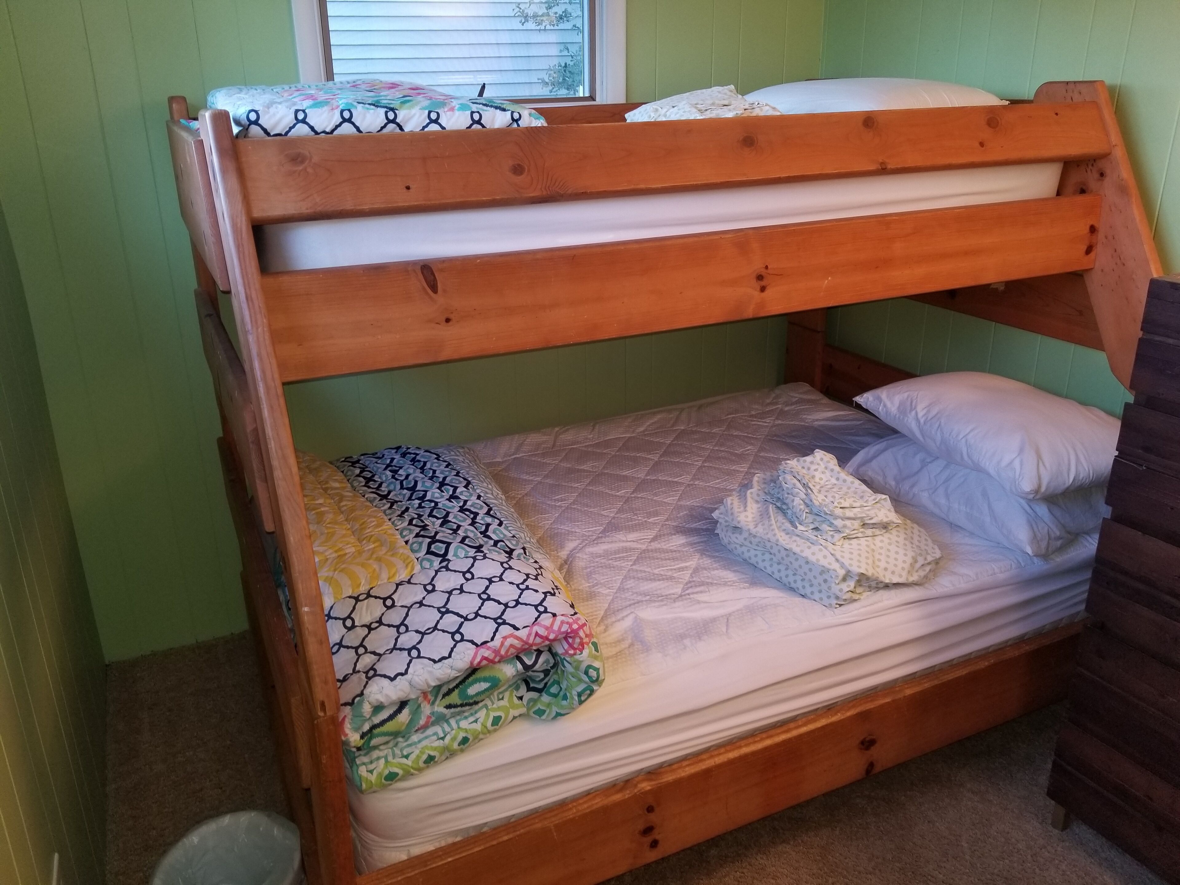 A bunk bed with a quilted mattress and pillows, a wooden headboard, and a window with blinds.