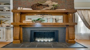 A fireplace with a brick surround, a mantel with decorative items, and a tiled floor.