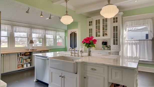 A kitchen with white cabinets, a large island, and a window with white curtains.