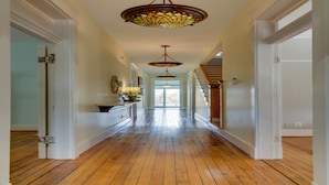 A hallway with wooden floors, white walls, and a staircase leading to a second floor.