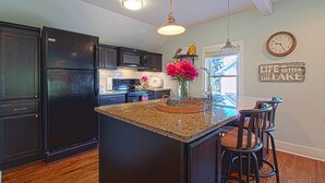 A kitchen with dark cabinets, a black refrigerator, granite countertops, and a central island with bar stools.