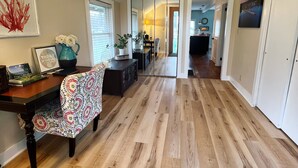A spacious hallway with wooden flooring, a dining area with a patterned chair, and a mirror wall.