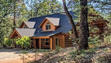 A log cabin with a steeply pitched roof, a front porch, and a dirt driveway.