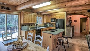 A wooden cabin kitchen with a large island, wooden cabinets, and a view of the forest.