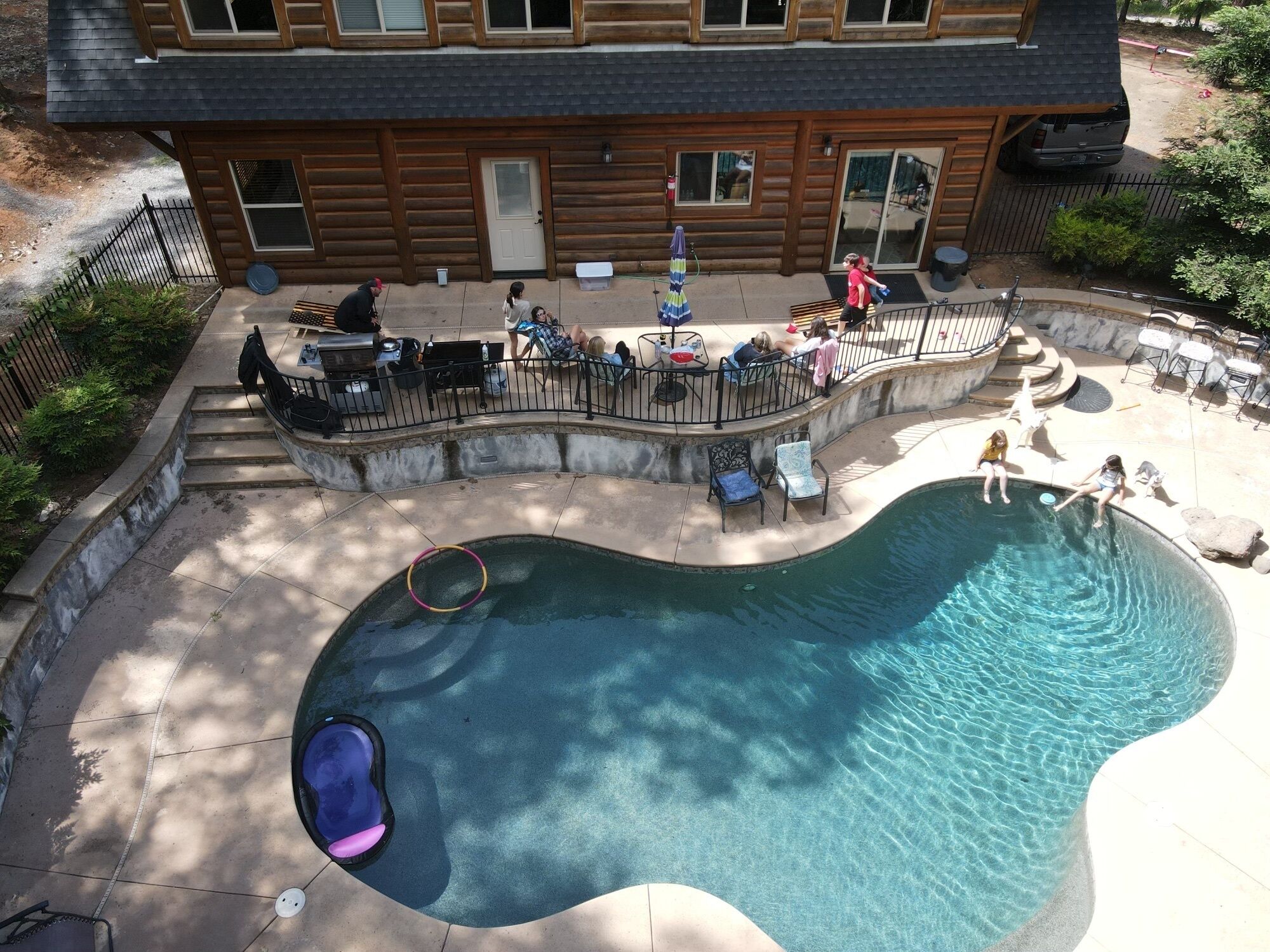 Ein Swimmingpool mit Rutsche, umgeben von einer Holzterrasse und einem eingezäunten Bereich mit Sitzgelegenheiten im Freien.