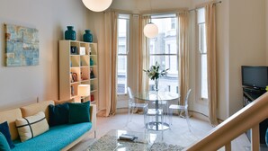 A modern living room with a teal sofa, a glass coffee table, a clear dining table with chairs, and a bookshelf. - LOCATION LOCATION LOCATION - Prime central London ZONE 1 (London)