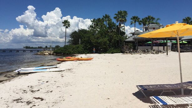 Una playa con kayaks, una sombrilla amarilla y sillas de descanso.