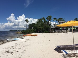 A beach with kayaks, a yellow umbrella, and lounge chairs.